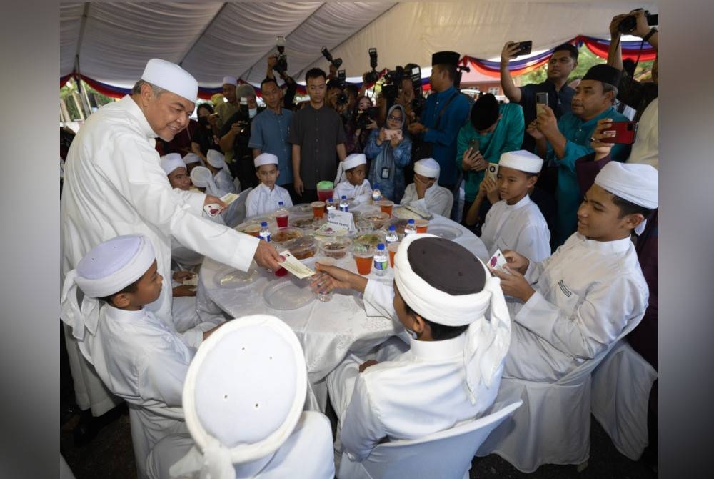 Ahmad Zahid (kiri) menyampaikan duit raya kepada para pelajar Tahfiz sempena majlis Santunan Kasih Ramadan KKDW di Pusat Transformasi ilmu Bukit Tiu hari ini. - Foto Bernama