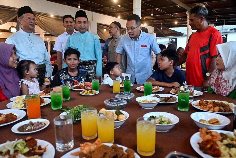 Nik Nazmi (berdiri, dua dari kanan) beramah mesra bersama golongan asnaf pada Majlis Iftar Ramadan di Batu Buruk Beach Resort pada Jumaat. - Foto Bernama