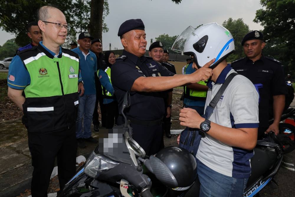 Kamarul Zaman Mamat (dua dari kiri) memakaikan topi keledar kepada penunggang motosikal pada Program Keselamatan Jalan Raya, Jabatan Siasatan dan Penguatkuasaan Trafik, bersama Perkeso di Plaza Tol Perling hari ini. - Foto Bernama