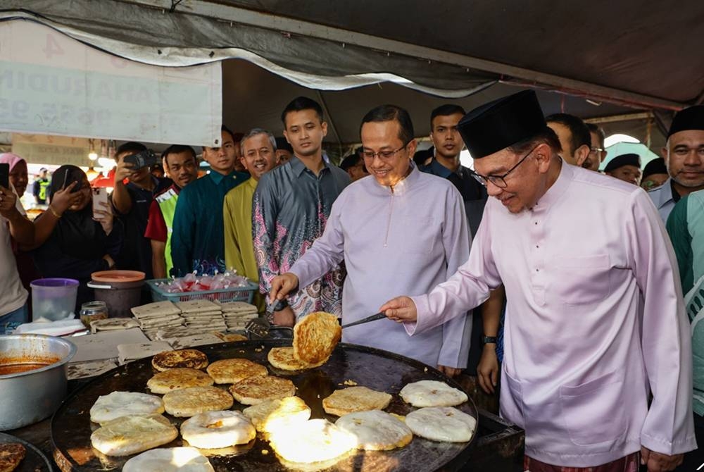 Anwar (kanan) mengalihkan murtabak semasa turun padang menyantuni orang ramai dan peniaga di Bazar Ramadan Gong Badak pada Sabtu. Turut sama Ahmad Samsuri (dua dari kanan). - Foto Bernama