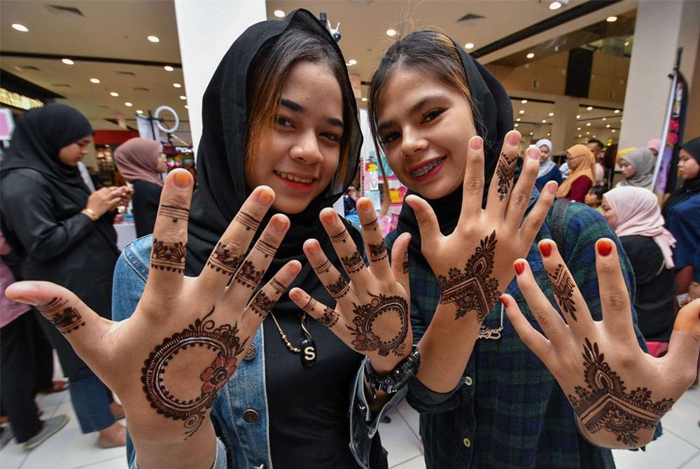 Nor Ain Natasha Rosli, 17, (kanan) bersama Noraina Natasha Mat Salleh, 17, (kiri) menunjukkan ukiran inai pada tangan yang dibuat mereka ketika keluar membeli-belah untuk membuat persiapan terakhir menjelang sambutan Aidilfitri di sebuah pasar raya hari ini. - Foto Bernama