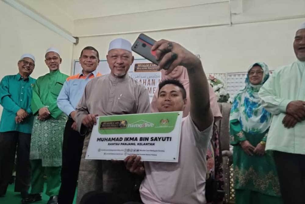 Mohamad Ikma mengambil peluang berswafoto bersama Ahmad ketika menyerahkan kunci rumah pada Majlis Serahan Kunci 10 Rumah &#039;Home2Live&#039; di Pusat Latihan dan Aktiviti Komuniti Rantau Panjang pada Rabu.