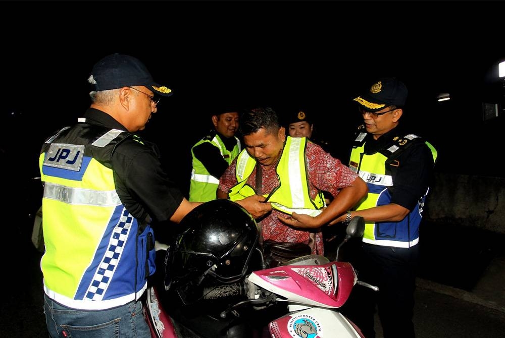 IPOH, 26 April -- Pengarah Bahagian Penguatkuasa Jabatan Pengangkutan Jalan (JPJ), Datuk Lokman Jamaan (kiri) memakaikan ves keselamatan kepada seorang penunggang motosikal ketika Operasi Bersepadu Sempena Hari Raya Aidilfitri (HRA) 2023 di Jalan Kuala Kangsar, malam Rabu. - Foto Bernama