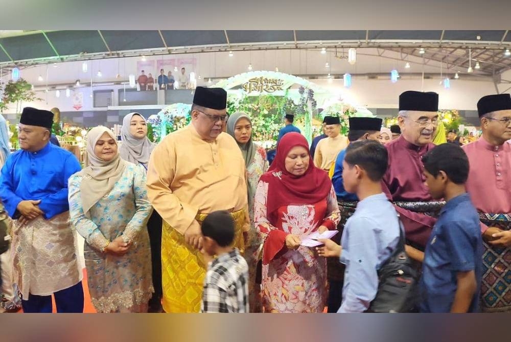 Ab Rauf (tiga dari kiri) bersama Asmah (empat dari kiri) dan Mohd Ali ketika memberikan duit raya kepada orang ramai yang hadir ke Majlis Rumah Terbuka Aidilfitri Kerajaan Negeri Melaka di MITC, Ayer Keroh pada Sabtu.