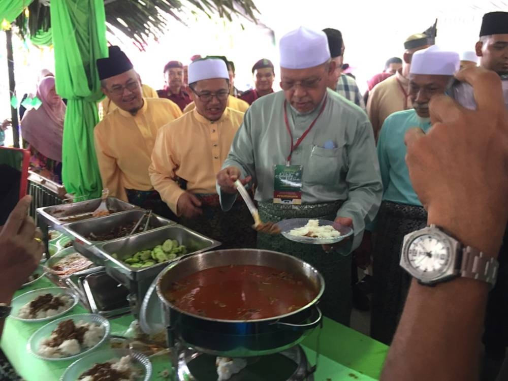 Ahmad (kanan) mengambil gulai daging kawah yang disediakan di Majlis Rumah Terbuka Aidilfitri Pas Kelantan. 