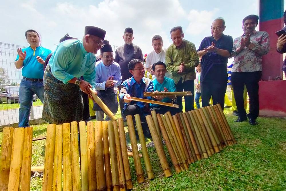 Kon Yeow (duduk, kiri) membuka lemang yang dibakar pada Majlis Rumah Terbuka Aidilfitri Parlimen Batu Kawan dan Kawasan Dewan Undangan Negeri (DUN) Bukit Tambun di Taman Tangling, pada Sabtu.