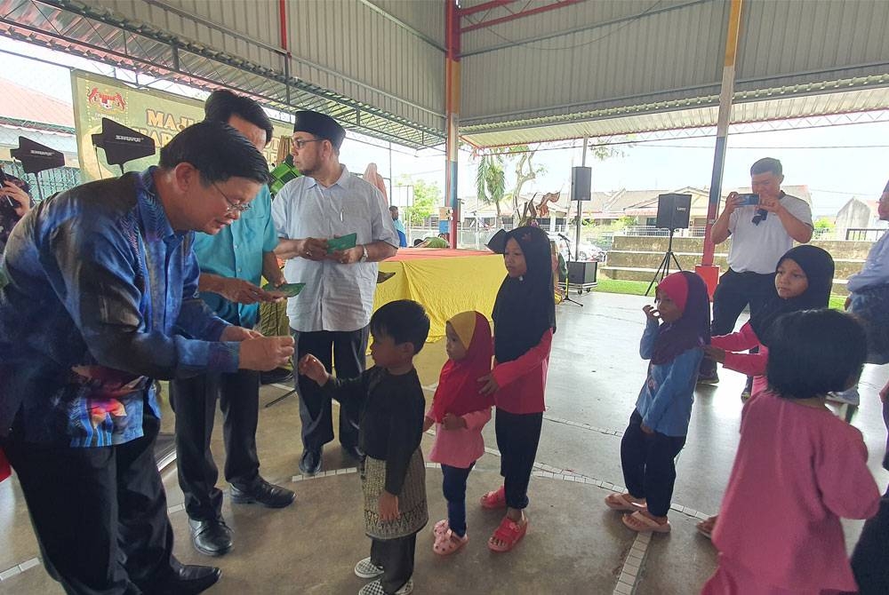 Kon Yeow (kiri) menyampaikan duit raya kepada kanak-kanak yang hadir pada Majlis Rumah Terbuka Aidilfitri Parlimen Batu Kawan dan Kawasan Dewan Undangan Negeri Bukit Tambun di Taman Tangling, pada Sabtu.