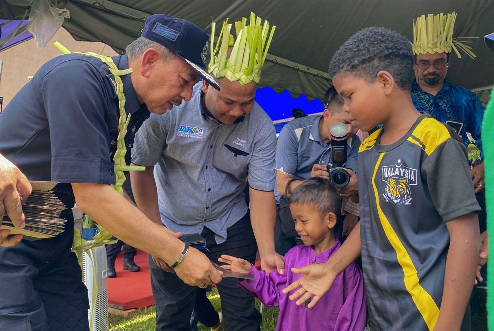 Muhamad Zaki (kiri) menyampaikan sumbangan kepada sebahagian kanak-kanak masyarakat Orang Asli suku kaum Mendriq dan Bateq di Kampung Pasir Linggi pada Ahad. - Foto Bernama