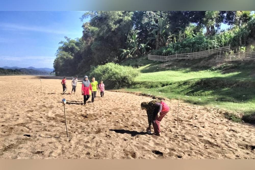 Kanak-kanak bermain bola di permukaan pasir yang melebar akibat kemarau.