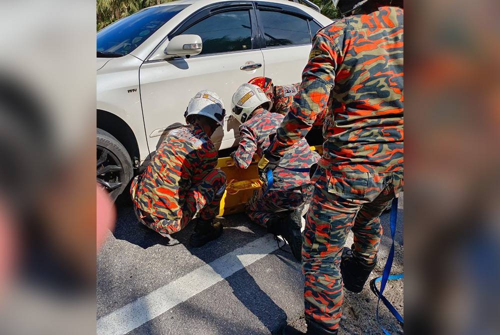 Anggota bomba mengeluarkan seorang lelaki warga Pakistan yang terperosok bawah kereta dalam kemalangan di Jalan Bypass Kota Tinggi, Kota Tinggi pada Isnin.