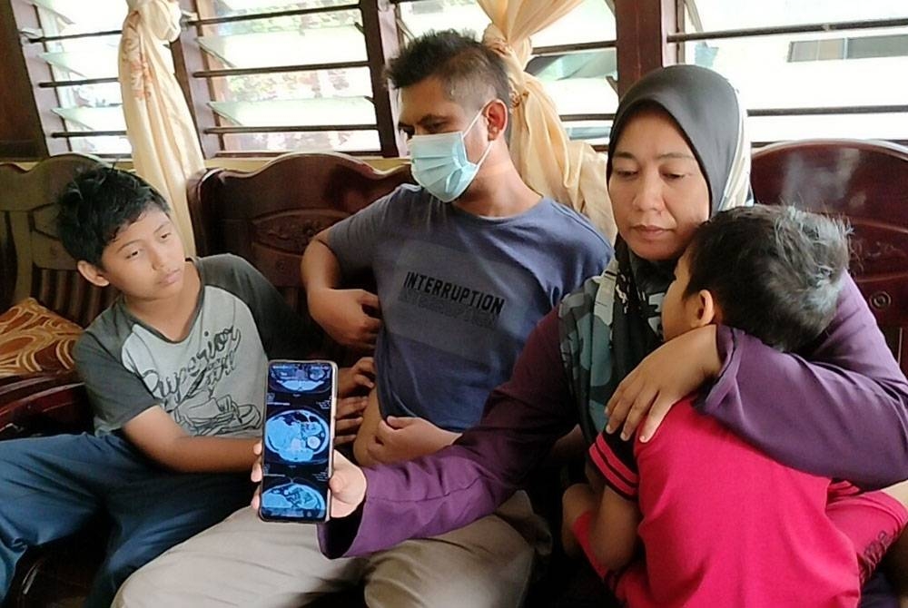 Suhana (tiga tiga dari kiri) menunjukkan imbasan x-ray kanser buah pinggang suaminya, Megat Asraff (dua dari kiri) ketika ditemui di kediamannya di Kampung Gelam.