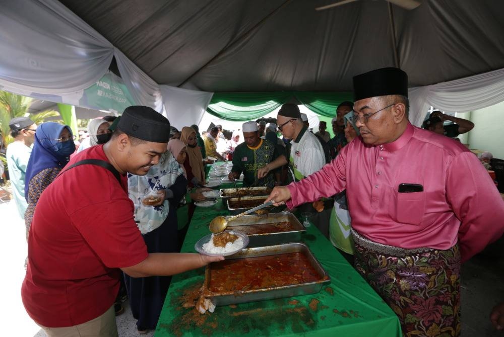 Sanusi (kanan) mencedok lauk kepada pengunjung yang hadir Majlis Rumah Terbuka Aidilfitri Pas Pusat di Kompleks Pas Kedah, Kota Sarang Semut pada Sabtu.