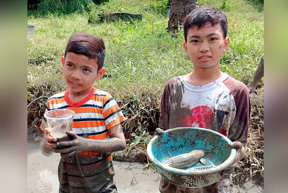 Ahmad Zawawi (kiri) dan rakannya, Muhammad Irfan Firdaus menunjukkan ikan yang berjaya ditangkap ketika menyertai program Ngoca di Tebong, Alor Gajah pada Ahad. - Foto Bernama