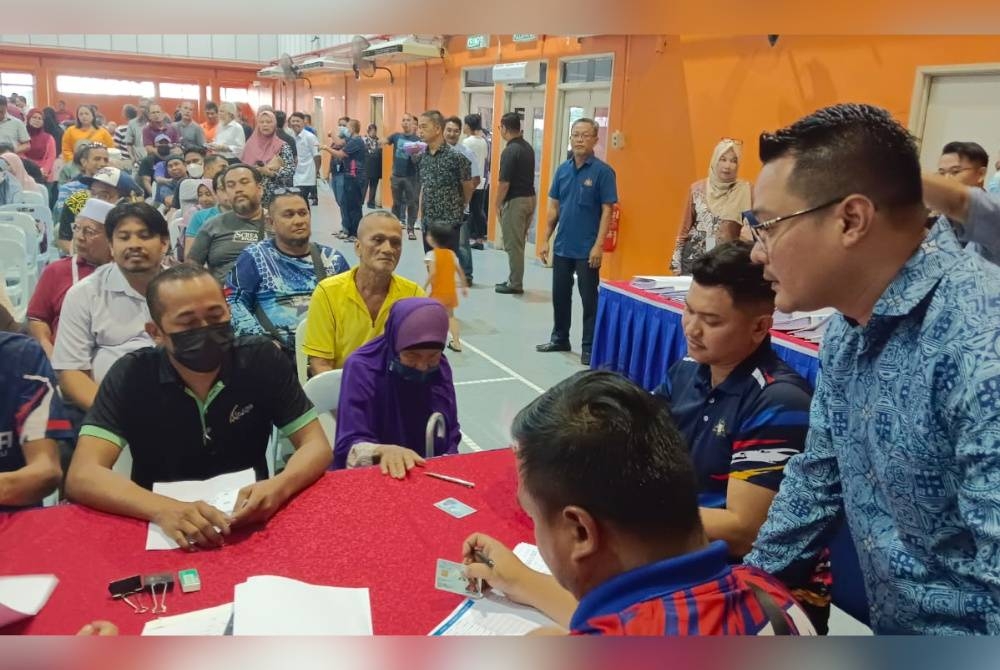 Mohd Hairi ( kiri) meninjau proses penyerahan bantuan kepada mangsa di Dewan Kampung Melayu Majidee pada Khamis.