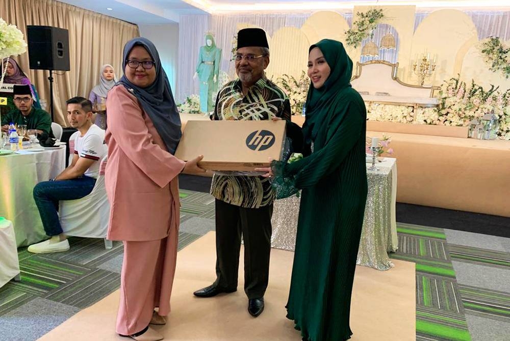 Tajuddin (tengah) bersama Tina (kanan) menyampaikan set komputer riba kepada pelajar TIC sempena majlis Rumah Terbuka Aidilfitri TT Group Companies pada Ahad.