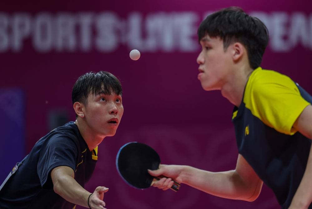 Aksi Javen (kanan) dan Qi Shen (kiri) ketika menentang regu Singapura dalam perlawanan akhir ping pong regu lelaki pada Sukan SEA 2023 Kemboja di Stadium Badminton Morodok Techo pada Ahad. - Foto Bernama