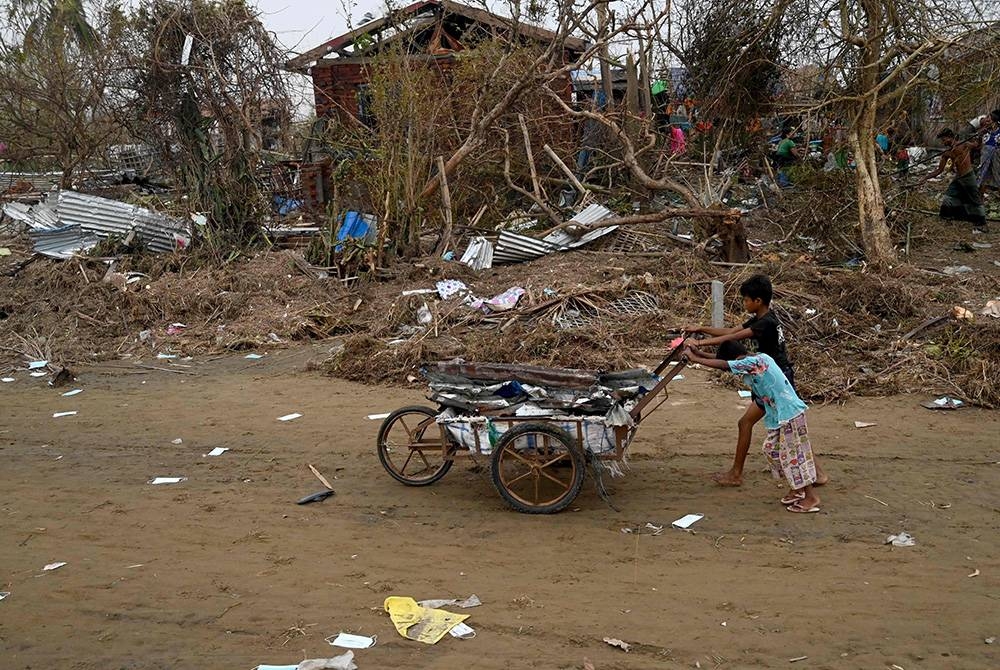 Kanak-kanak menolak kereta tolak yang penuh dengan serpihan di kem pelarian Khaung Dote Khar Rohingya di Sittwe, di negeri Rakhine Myanmar pada Isnin selepas dilanda Siklon Mocha. - Foto AFP