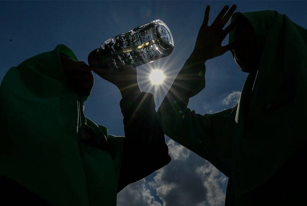 Pelajar sekolah menikmati air minuman di bawah terik matahari ketika tinjauan di sekitar pusat bandar. - Foto Bernama