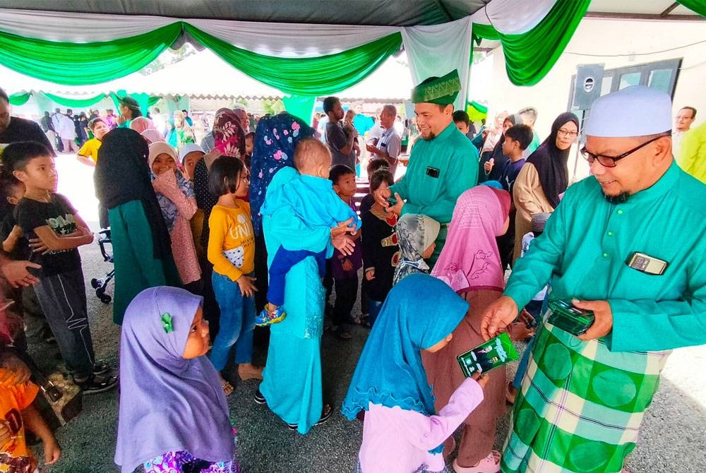 Rosli (kanan) dan Wan Razali menyampaikan duit raya kepada kanak-kanak pada Majlis Jamuan Aidilfitri di Dewan Serbaguna Inderapura, Kuantan pada Sabtu.