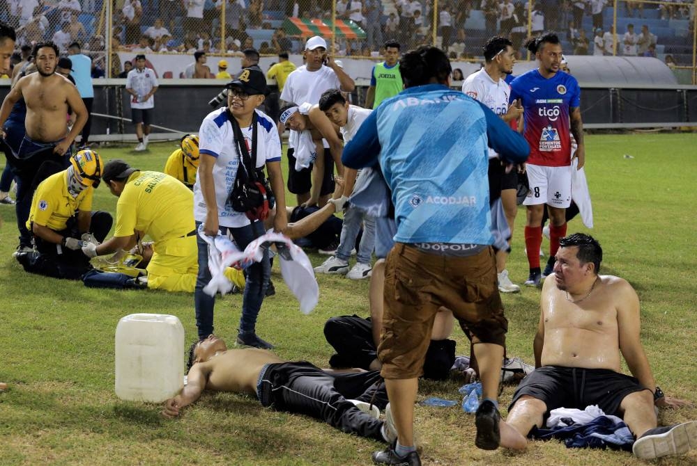 Penyokong yang cedera dibantu oleh orang lain berikutan rempuhan semasa perlawanan bola sepak antara Alianza dan FAS di stadium Cuscatlan di San Salvador, pada Sabtu. - Foto AFP