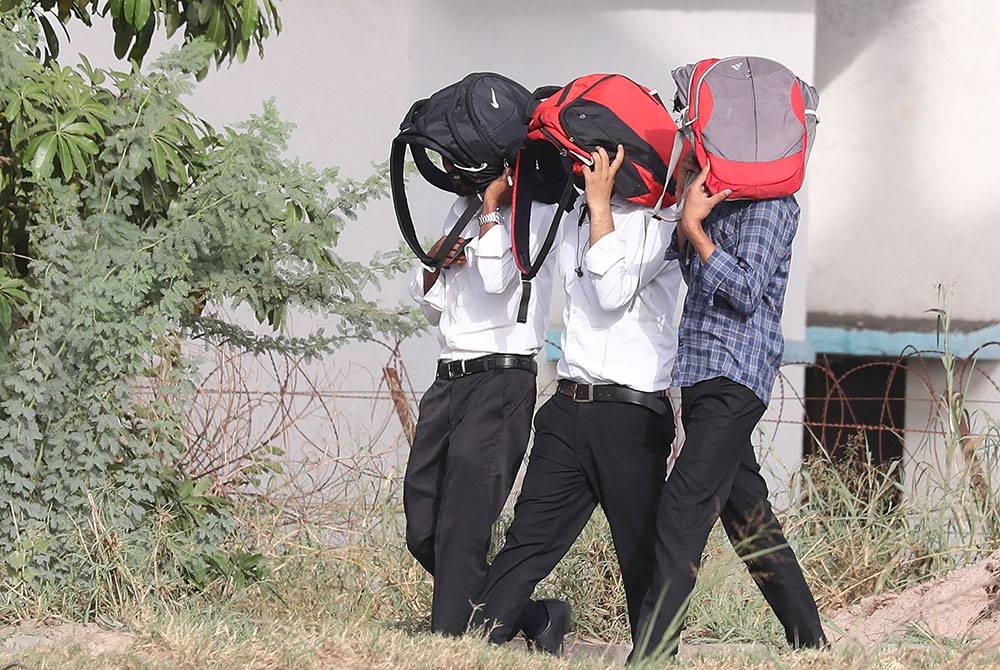 Pelajar menggunakan beg sekolah untuk melindungi diri mereka daripada matahari semasa gelombang panas di New Delhi, India pada Isnin. - Foto EPA