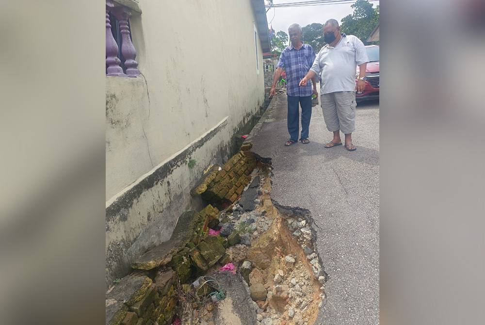 Ismail (kanan) dan Maran menunjukkan tebing jalan yang runtuh sejak empat bulan lalu yang dilihat mampu mengundang bahaya kepada orang ramai di Jalan Bakawali 25, Taman Johor Jaya, Johor Bahru pada Sabtu