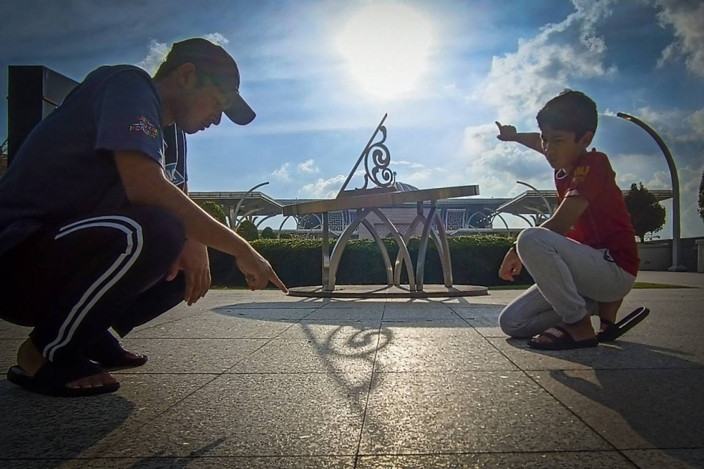 Izz Harraz Izqandar bersama adiknya Izz Husayn Izqandar melihat arah bayang matahari dari jam matahari di Kiblat Walk bagi melihat arah kiblat dengan menggunakan kaedah Istiwa Adzam iaitu kaedah bayang matahari ketika matahari atas Kaabah hari ini pada jam 5.18 petang. - Foto Bernama