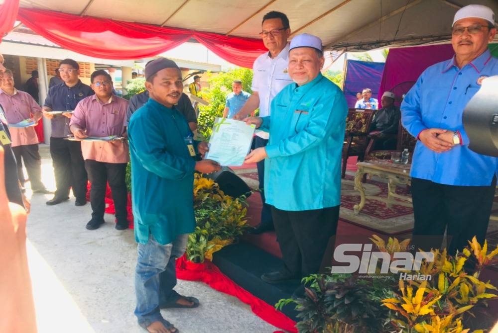 Nik Amar (dua dari kanan) menyampaikan geran tanah kepada penduduk di Tanah Merah.