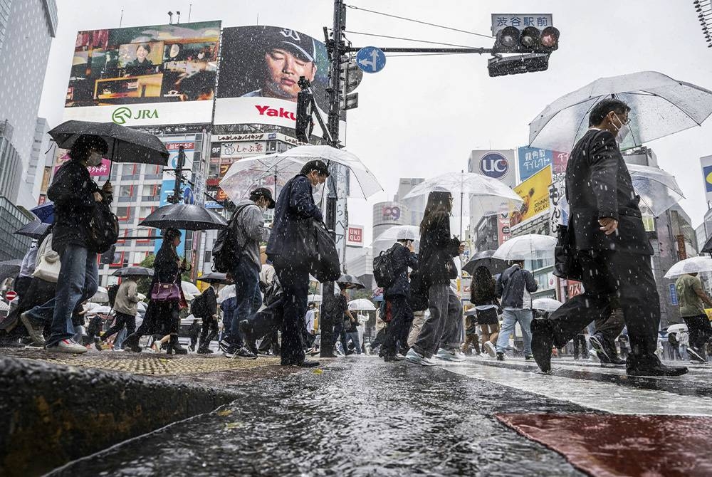 Orang ramai kelihatan menggunakan payung susulan hujan lebat di daerah Shibuya di Tokyo. - AFP