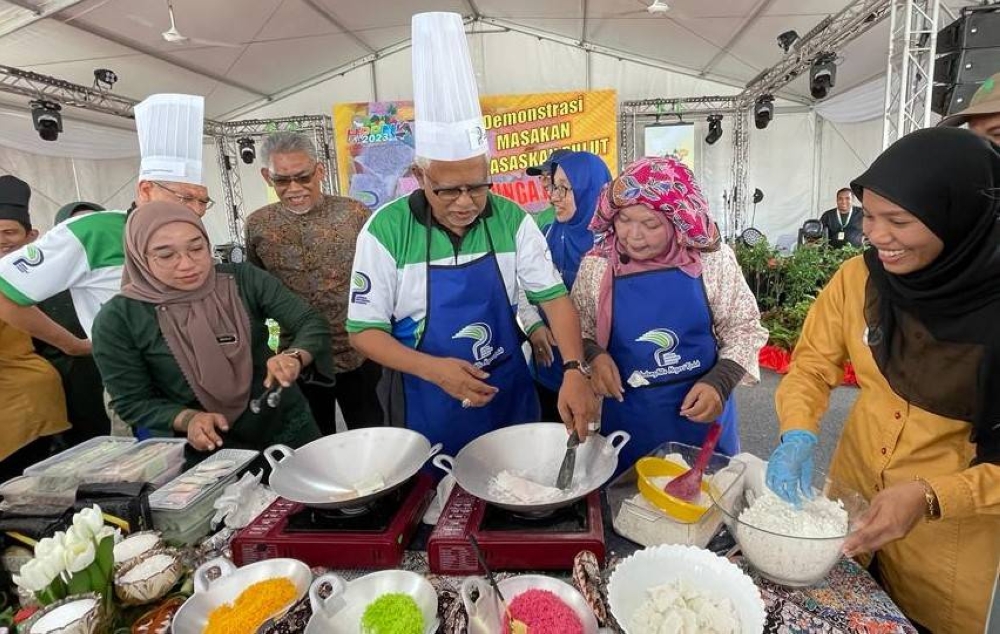 Mahfuz (tengah) turut memeriahkan demonstrasi masakan berasaskan pulut, iaitu bunga pudak ketika meninjau reruai LPP sempena HPPNK di perkarangan Stadium Darul Aman.