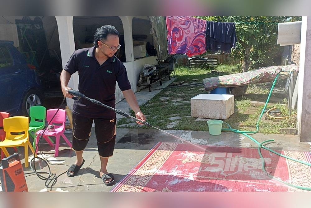 Mohd Shahid membersihkan tikar yang diselaputi lumpur akibat banjir yang berlaku pada Isnin.