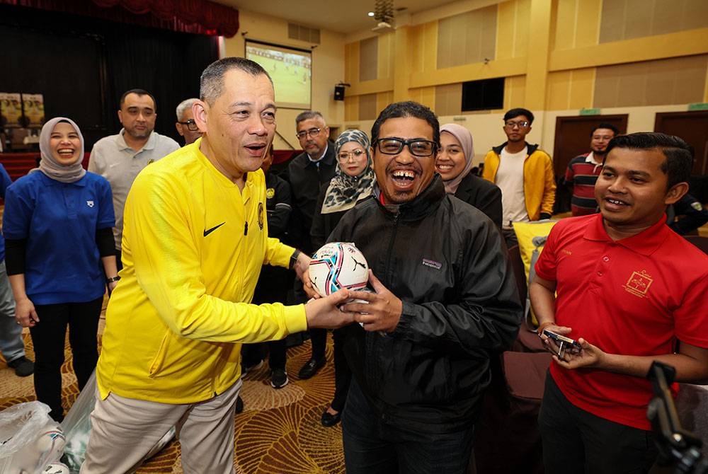 Hamidin (kiri) menyampaikan cenderahati kepada penyokong skuad Harimau Malaya pada Sesi Town Hall FAM malam tadi. - Foto Bernama