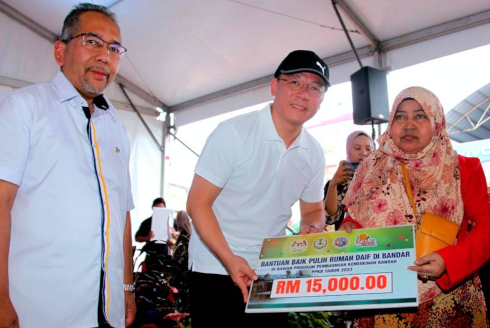 Kor Ming (tengah) menyampaikan replika bantuan baik pulih rumah daif bandar kepada penerima Jufinas Ibrahim (kiri) pada Program Fiesta Teluk Intan: Komuniti Bandar Dekat Di Hati di Dataran Menara Condong, Teluk Intan hari ini. - Foto Bernama