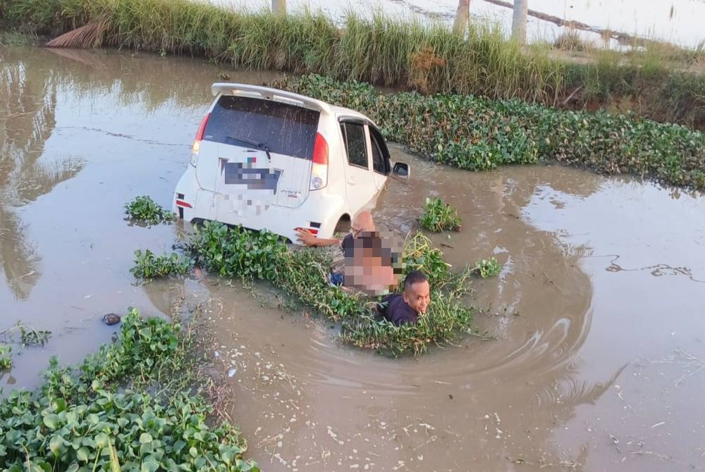 Dua anggota polis mengeluarkan suspek dari keretanya dalam tali air di Kampung Alor Besar, Alor Setar pada petang Isnin. - Foto PDRM