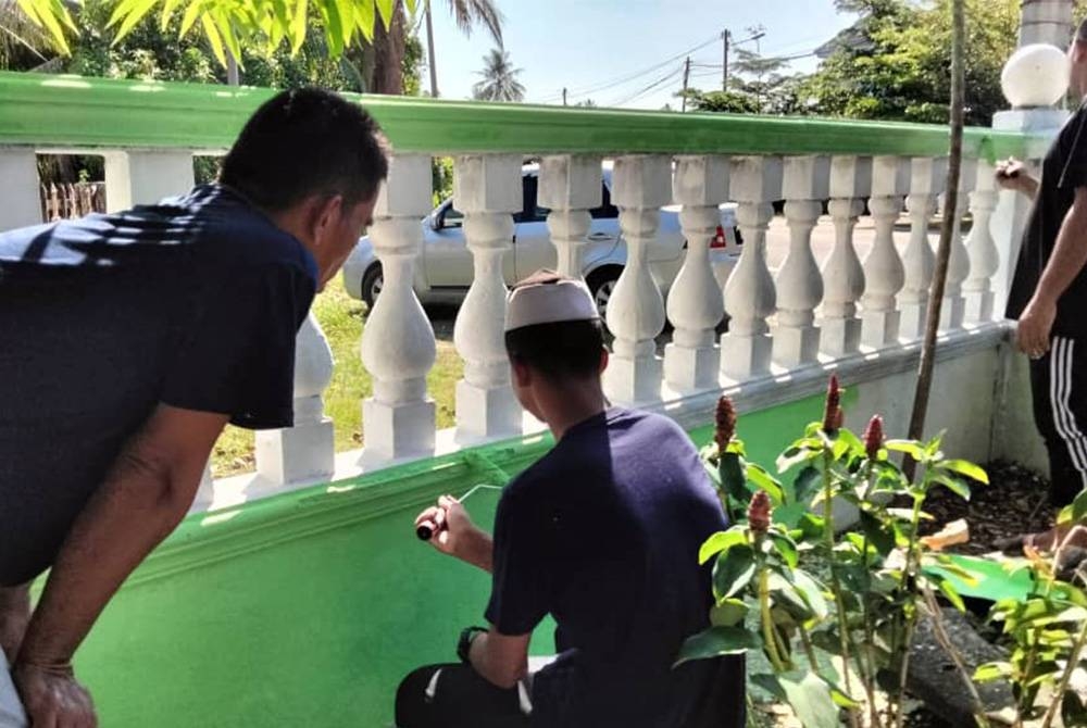 Izuan (tengah) mengecat pagar masjid pada Program CSR Penghuni Parol Bersama Ahli Jawatankuasa Masjid Kemumin, Pengkalan Chepa pada Jumaat.