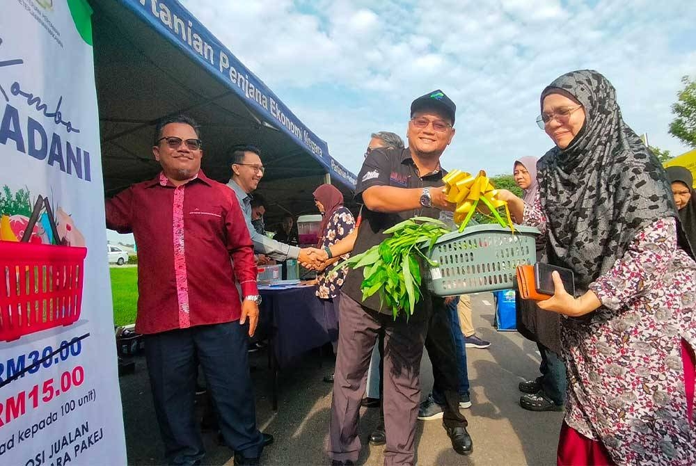 Saiful (tengah) menyampaikan bakul set bahan mentah berharga RM15 kepada pengguna terawal ke program Jualan Agro Madani dan majlis pelancaran medan jualan terus dari ladang (JTDL) dan GBBS FAMA di Tanah Putih di sini pada Sabtu.