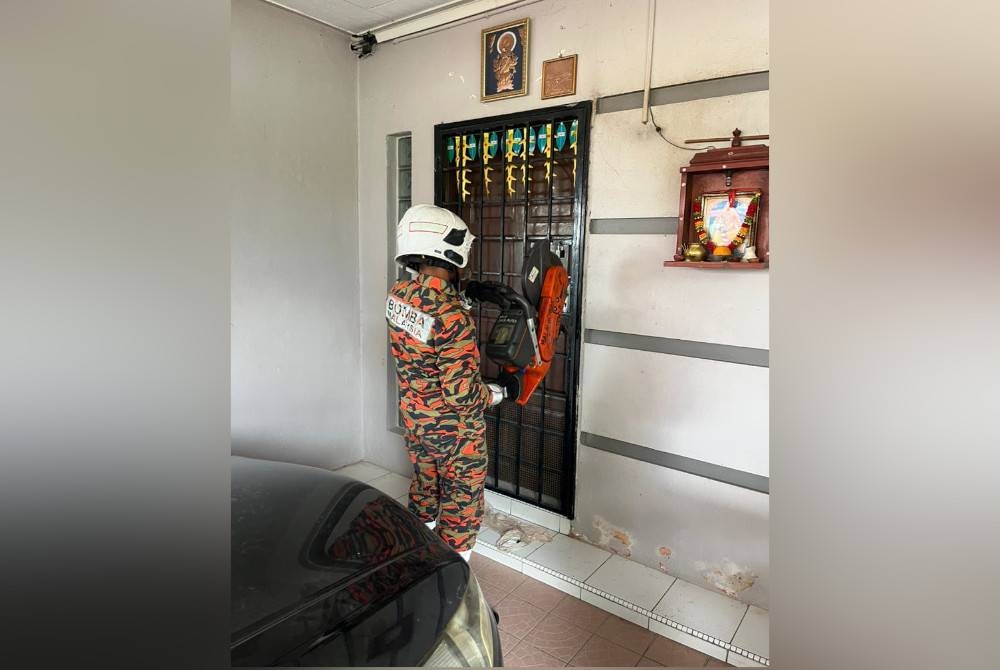 Anggota bomba menggunakan peralatan khas untuk membuka pintu rumah yang didiami warga emas berusia 77 tahun itu. - Foto ihsan Bomba Perak