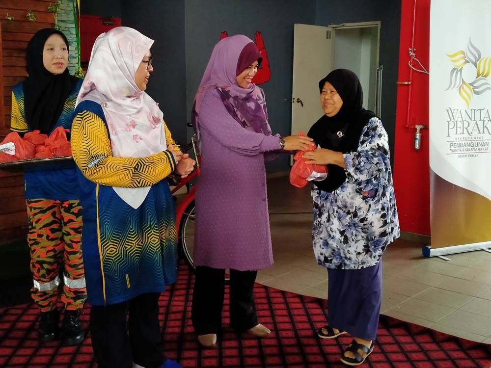 Sayani (tengah) menyampaikan daging korban kepada penerima sambil disaksikan Jamilah (kiri) sempena Program Imarah Aidiladha JBPM Perak di Balai Bomba dan Penyelamat Meru Raya di sini pada Jumaat.