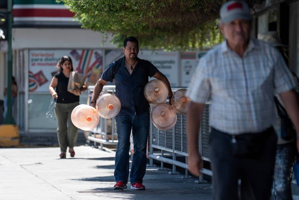 Seorang lelaki membawa botol-botol kosong untuk diisi air berikutan cuaca panas melampau di negeri utara Nuevo León, Mexico. - Foto EPA