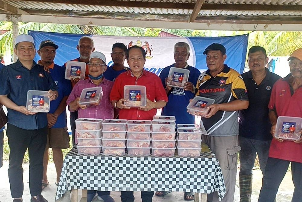 Ahmad ( tengah) bersama penduduk Kampung Parit Ibrahim mengagihkan daging korban pada Jumaat.