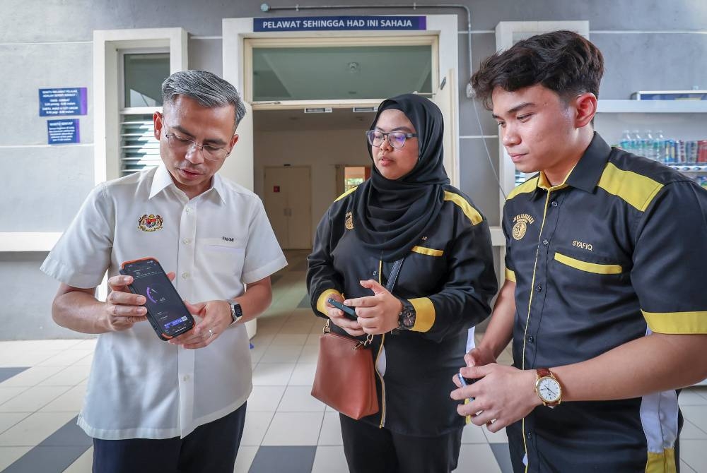 Fahmi Fadzil menunjukkan bacaan kelajuan internet pada telefon bimbitnya kepada pelajar (dari kanan) Muhammad Syafiq Akmal Mahadi dan Nur Amani Izzati Kamarul Azhar semasa meninjau keadaan internet di UiTM Kampus Dengkil pada Ahad. - Foto Bernama