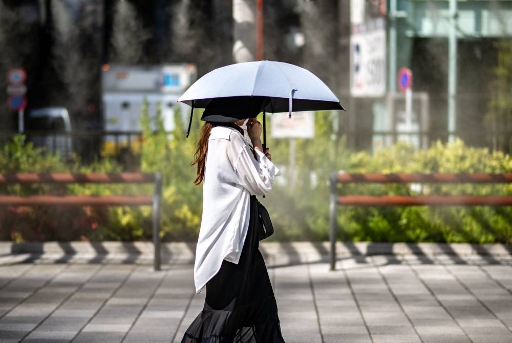 Seorang wanita berjalan dengan payung ketika cuaca panas terik di daerah Ginza di Tokyo pada Isnin. - Foto AFP