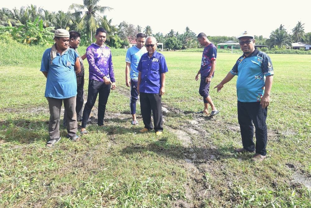 Maruwan (kanan) dan Mohd Shamsudin (tiga dari kanan) bersama penduduk menunjukkan permukaan padang rosak dan ditakungi air akibat kerja-kerja pembinaan pencawang.