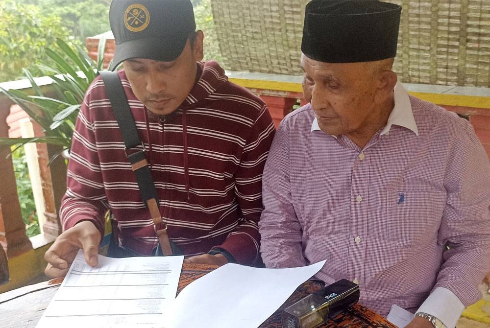 Tosrin (kanan) dan Khairol Nizam melihat penyata pinjaman peneroka di Felda Taib Andak pada Selasa.