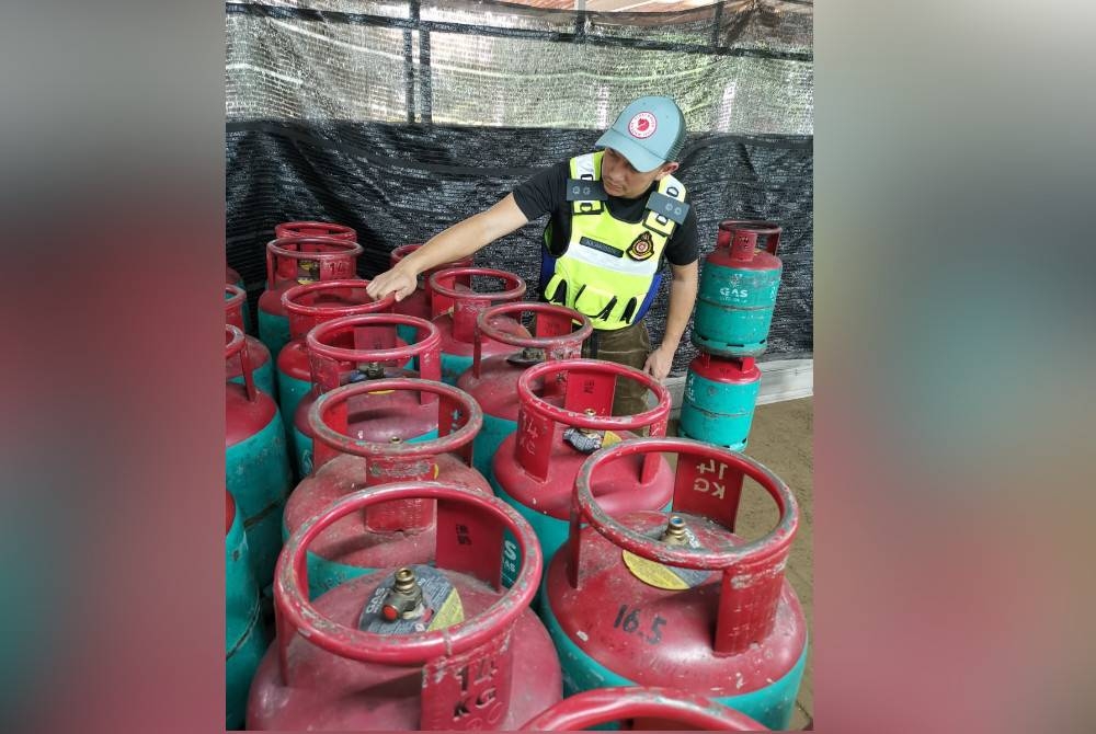 Anggota penguatkuasa KPDN menunjukkan antara tong gas LPG yang dirampas dalam serbuan itu.