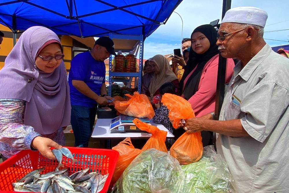 Fuziah (kiri) melayan pengunjung yang ingin mendapatkan barangan keperluan harian di Karnival Jualan Rahmah di Kampung Laut, Tumpat pada Jumaat.