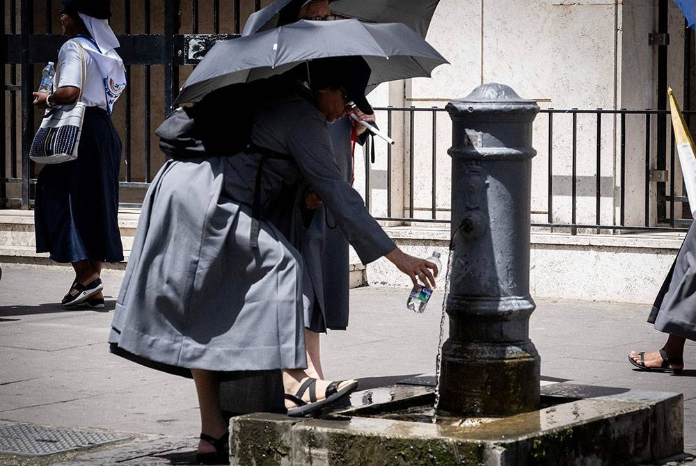 Seorang biarawati mengisi botolnya dengan air minuman dari air pancut di tengah Rom. Rom dijangka mencecah 43 darjah Celsius pada Isnin dan Selasa. - Foto AFP