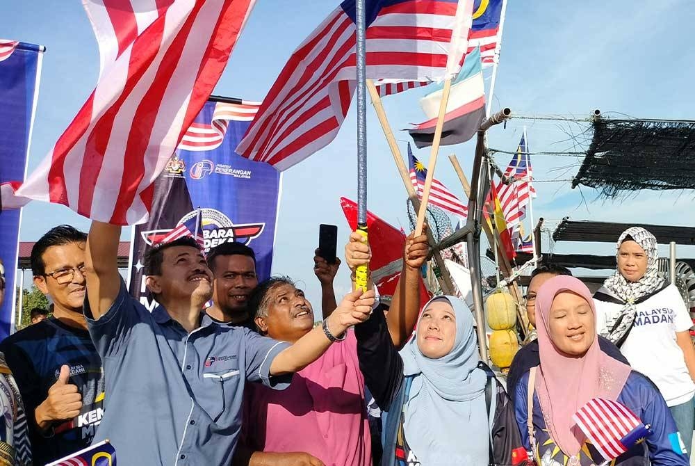 Sabri (kiri) menyerahkan Jalur Gemilang kepada Aidatul Shima (dua kanan) di Pasar Bisik Kuala Muda, Kedah.