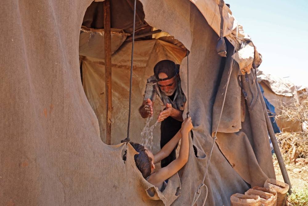 Seorang lelaki menuangkan air ke atas anaknya di dalam khemah mereka di kem Haranbush di wilayah Idlib pada Rabu. - Foto Mohammed Al-Rifai/ AFP