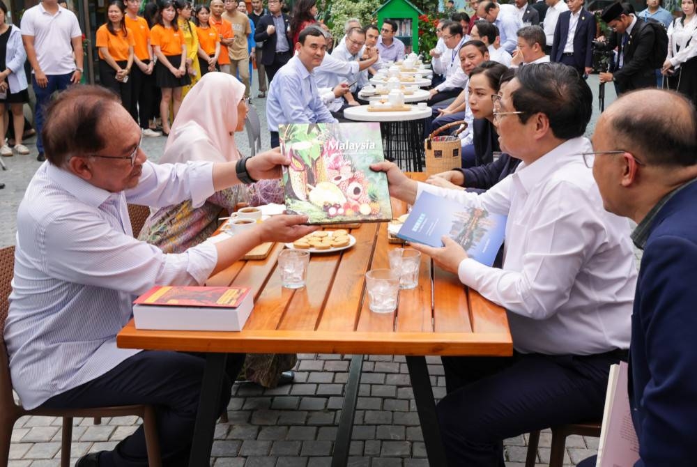 Anwar (kiri) bertukar buku dengan rakan sejawatnya, Pham Minh Chinh ketika melawat Book Street di Dinh Le Street hari ini. - Foto Bernama